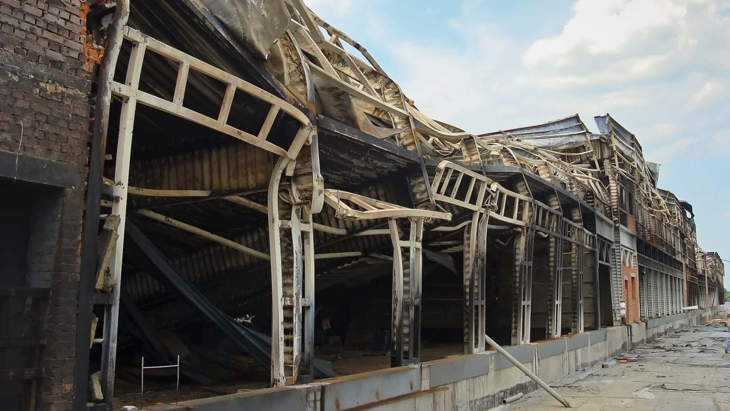 A dilapidated, burned-out warehouse with a partially collapsed roof and exposed structural elements.