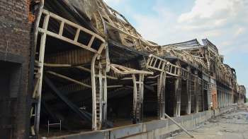A dilapidated, burned-out warehouse with a partially collapsed roof and exposed structural elements.