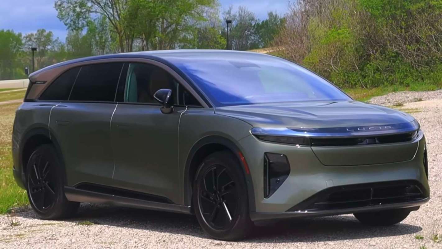 A green electric vehicle parked on a gravel surface with trees in the background.