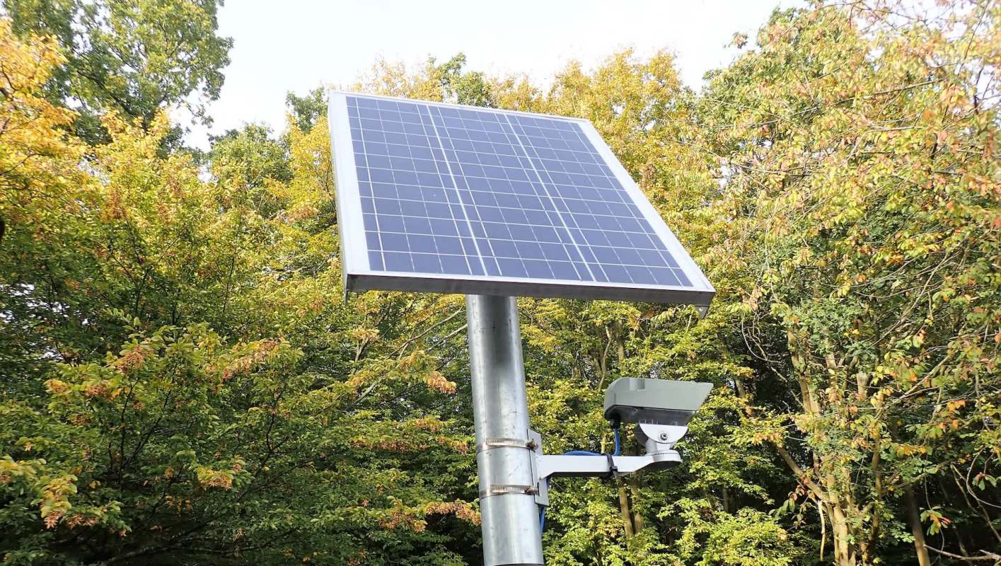 A solar panel mounted on a metal post surrounded by trees.