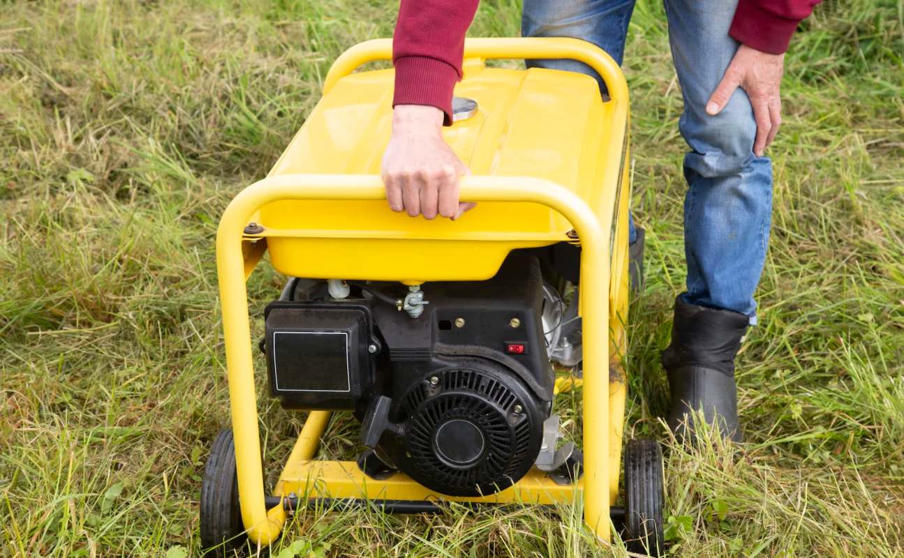A person holds the handle of a yellow generator on grass.