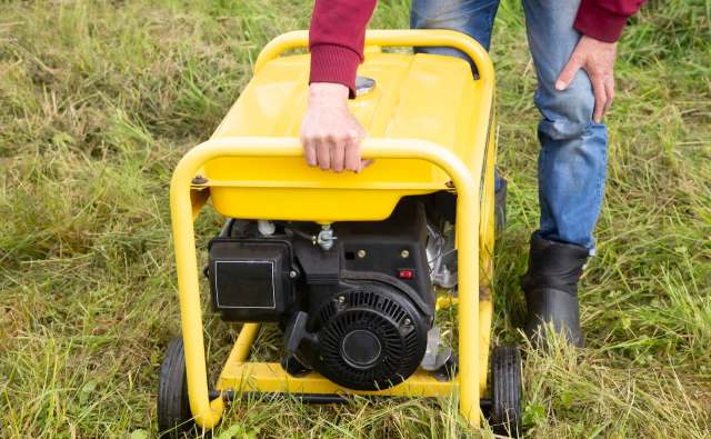A person holds the handle of a yellow generator on grass.