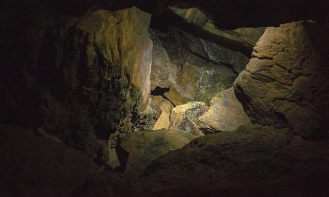 A dimly lit cave with various rock formations and surfaces illuminated by a small light source.