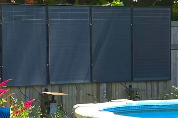 Solar panels installed beside a swimming pool, surrounded by plants and a wooden fence.