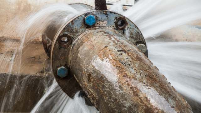 A metal pipe with rust, leaking water from a flange connection.