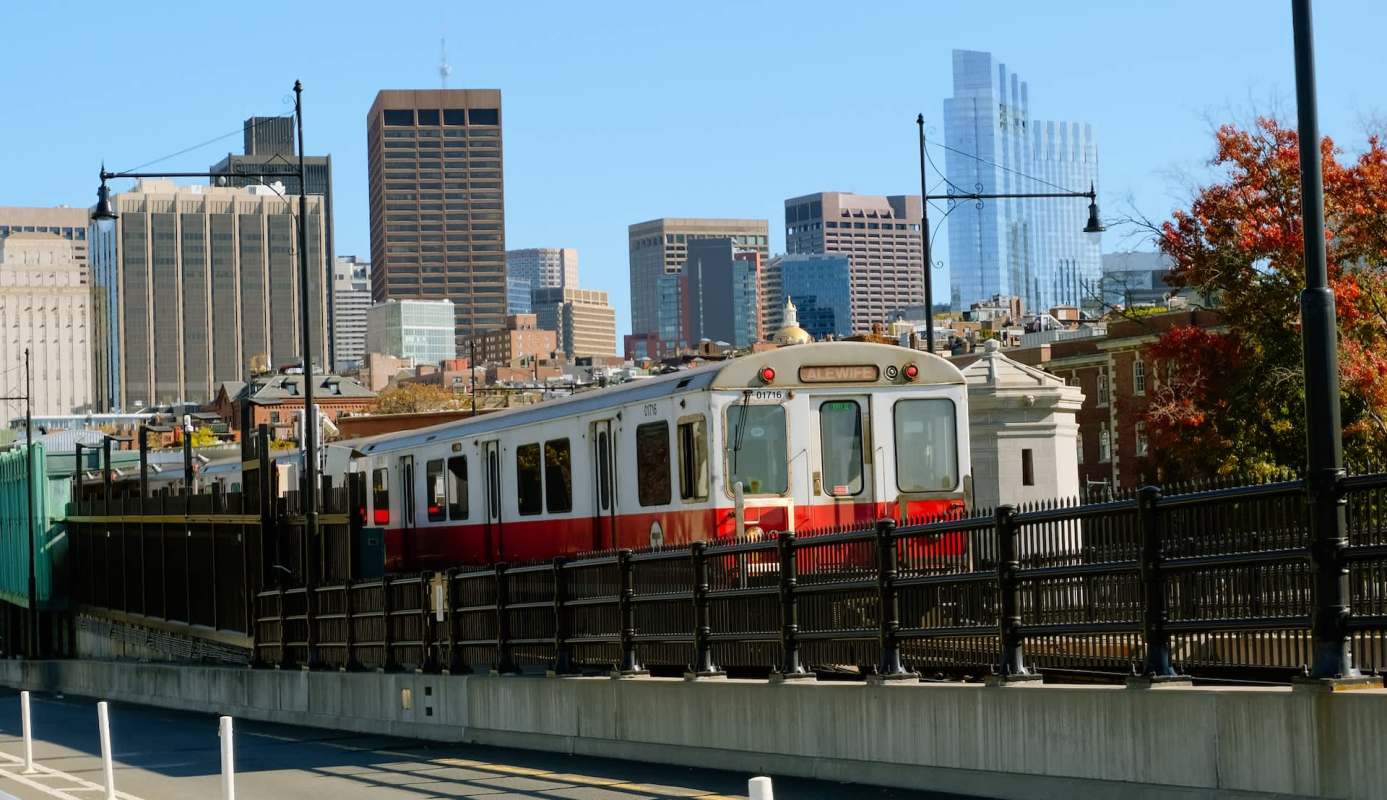 A train travels on an elevated track with a city skyline in the background.
