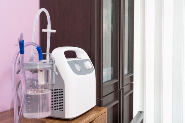 A medical device with a collection chamber and tubing on a wooden surface against a pink wall.