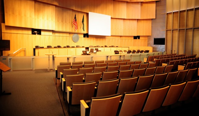 An empty courtroom with tiered seating, a large screen, and flags on display.
