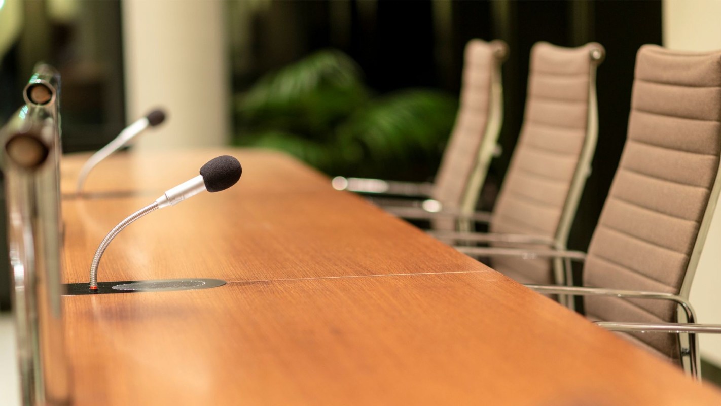 A conference table with microphones and empty chairs in a meeting room.
