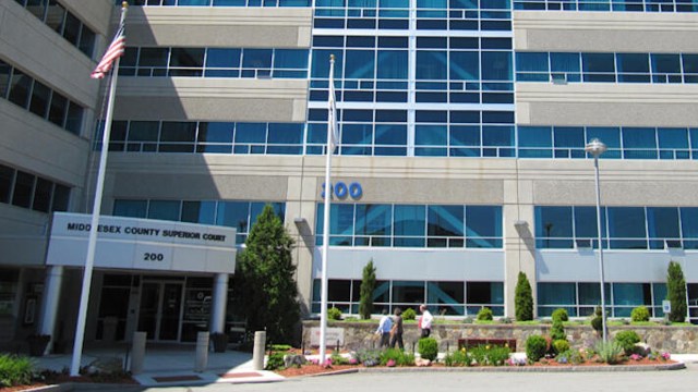 The entrance of the Middlesex County Superior Court building with flags and landscaped surroundings.