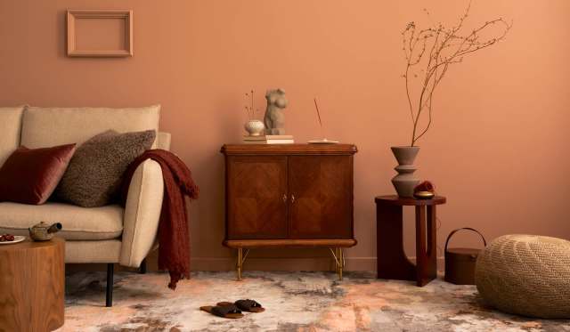 A cozy living room with a sofa, decorative pillows, a wooden cabinet, and various decorative items against a peach wall.