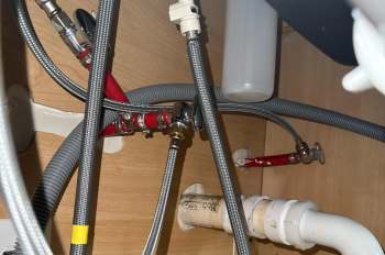 Piping and water supply connections under a sink, featuring braided hoses and red valves.