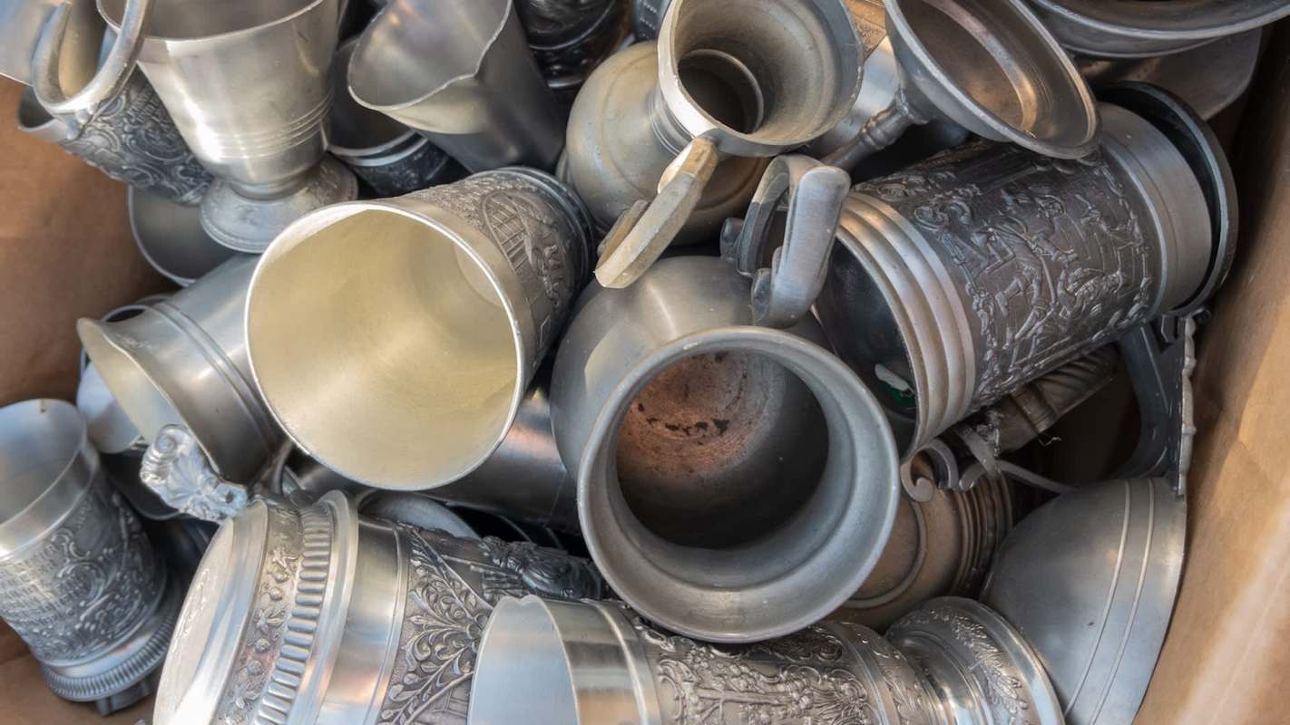 A collection of various metal cups and mugs piled in a box.