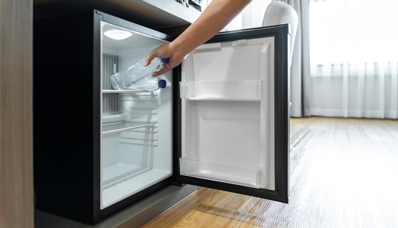 A person places a water bottle into the open compartment of a refrigerator.