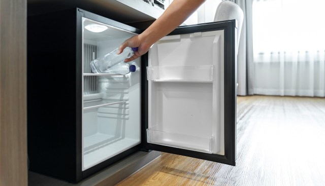 A person places a water bottle into the open compartment of a refrigerator.