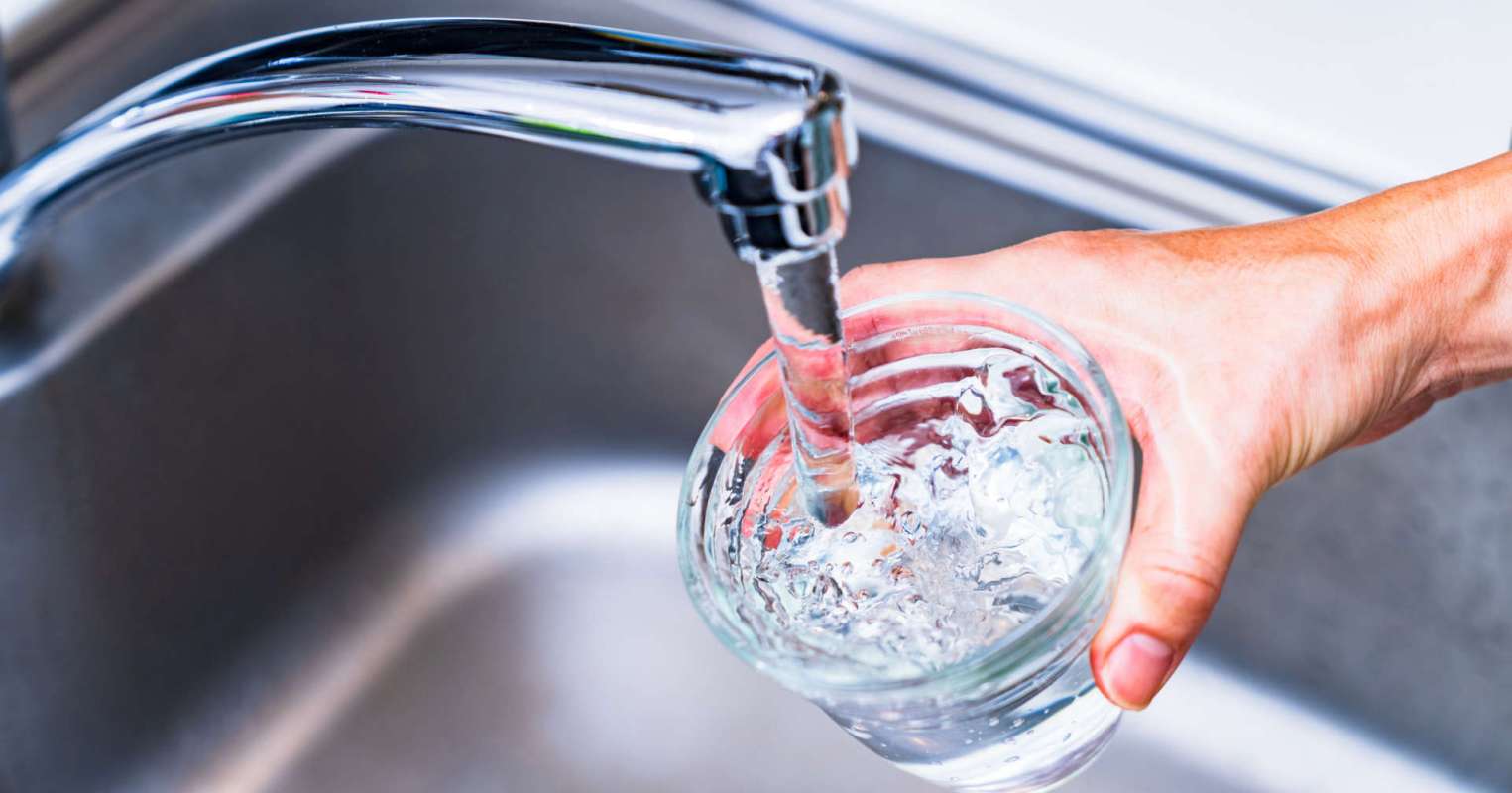 A hand holds a glass as water flows from a kitchen faucet into it.