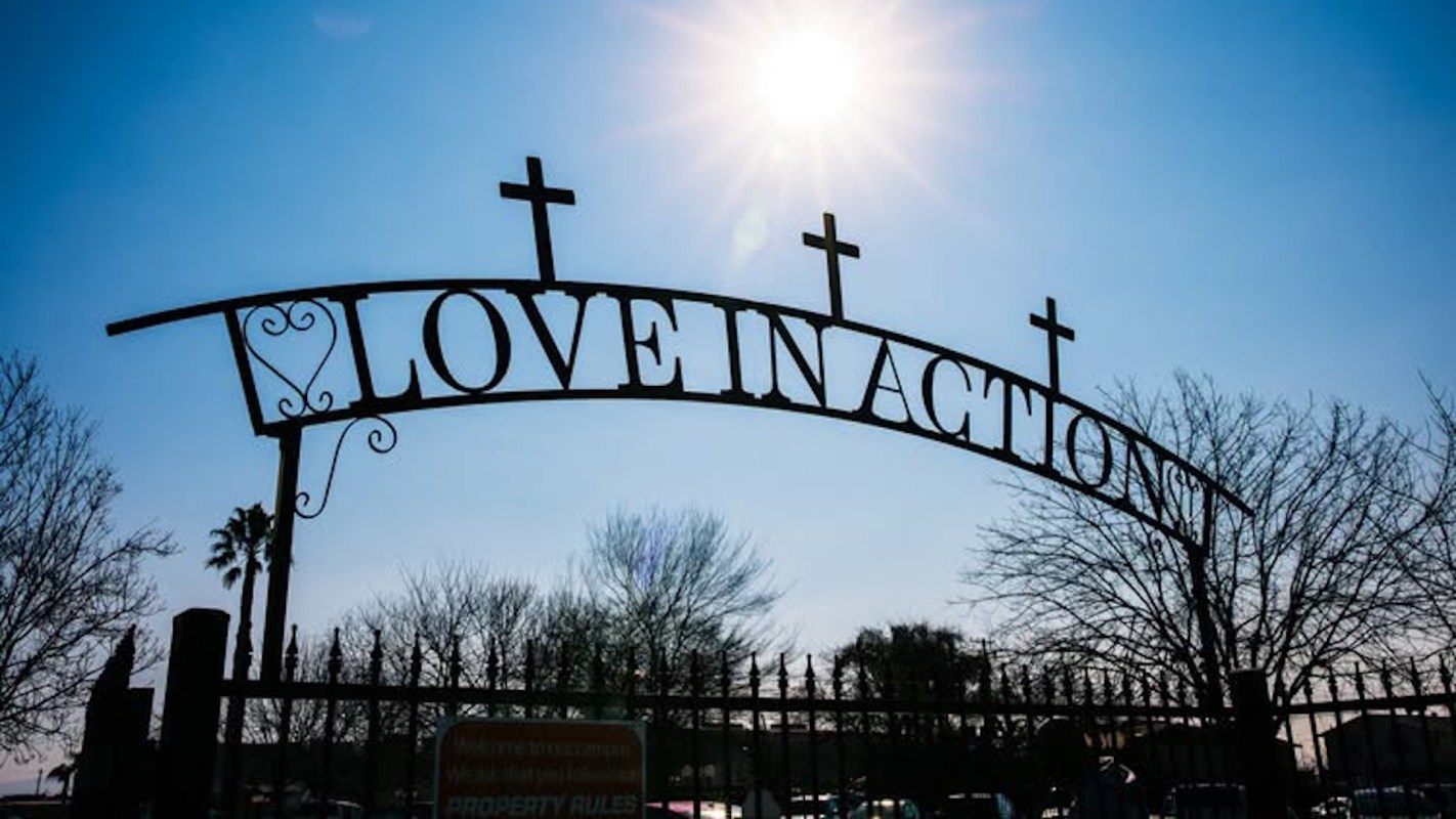 A metal archway with the words "LOVE IN ACTION" and three crosses against a clear blue sky.