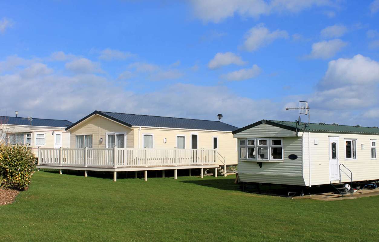 Two mobile homes are set on a grassy area under a partly cloudy sky.