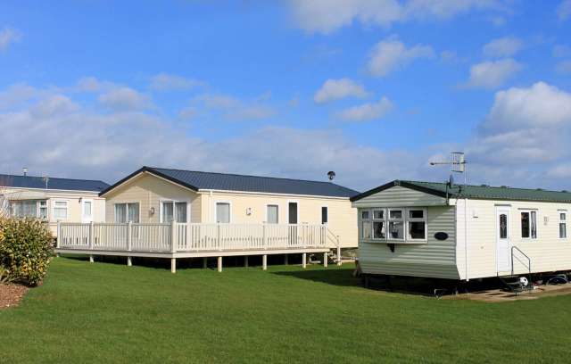 Two mobile homes are set on a grassy area under a partly cloudy sky.