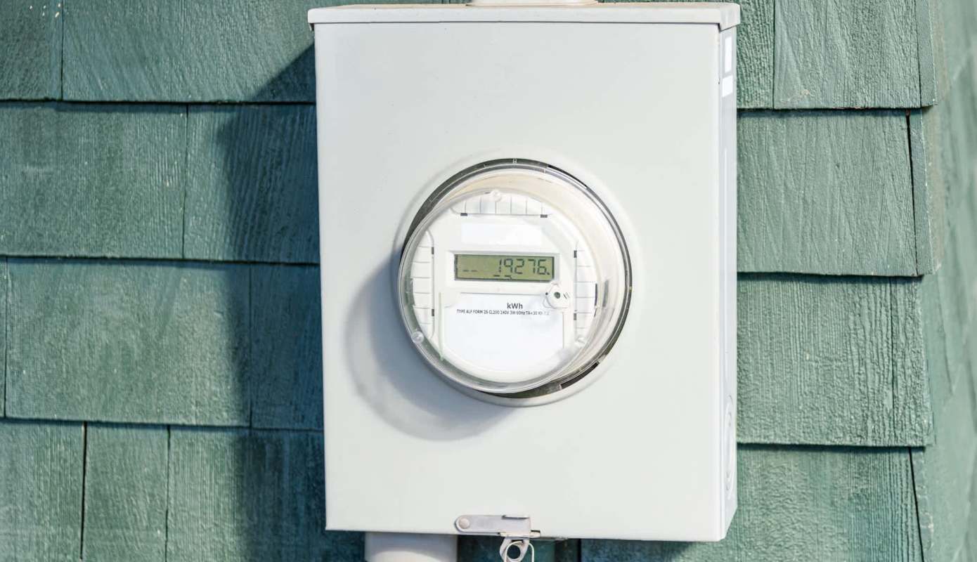 An electric meter mounted on a green wooden wall.