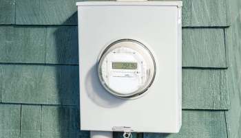 An electric meter mounted on a green wooden wall.