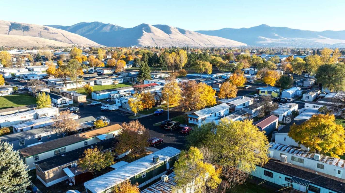 Aerial view of a mobile home park surrounded by autumn trees and mountains in the background.