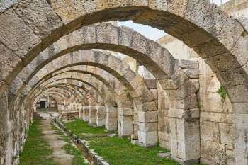 An interior view of stone arches in a historic ruin, with a pathway and grass in the foreground.