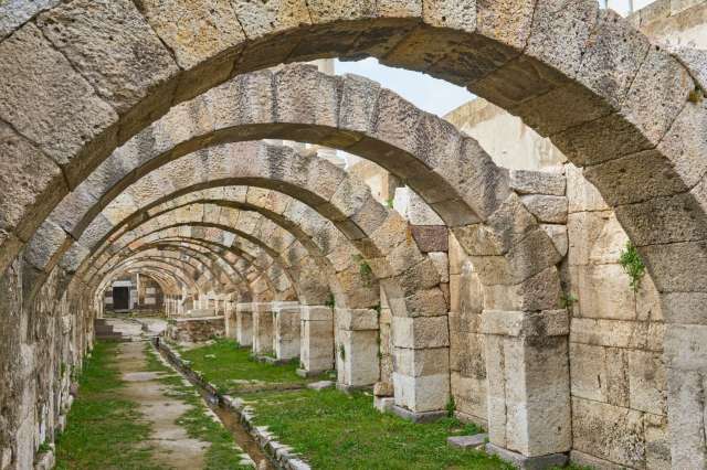 An interior view of stone arches in a historic ruin, with a pathway and grass in the foreground.