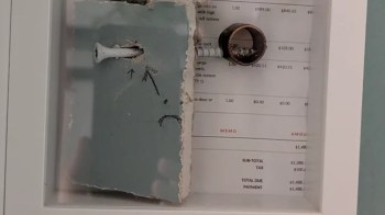 A damaged wall section with a visible screw and a circular pipe next to a printed invoice.