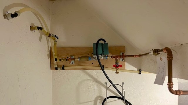 A wall-mounted plumbing setup with various pipes, valves, and a water pump.