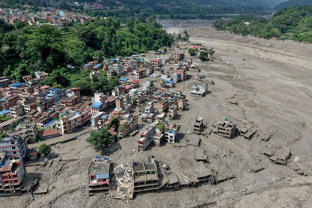 An aerial view of houses partially submerged in muddy water along a riverside after flash floods in Nepal.