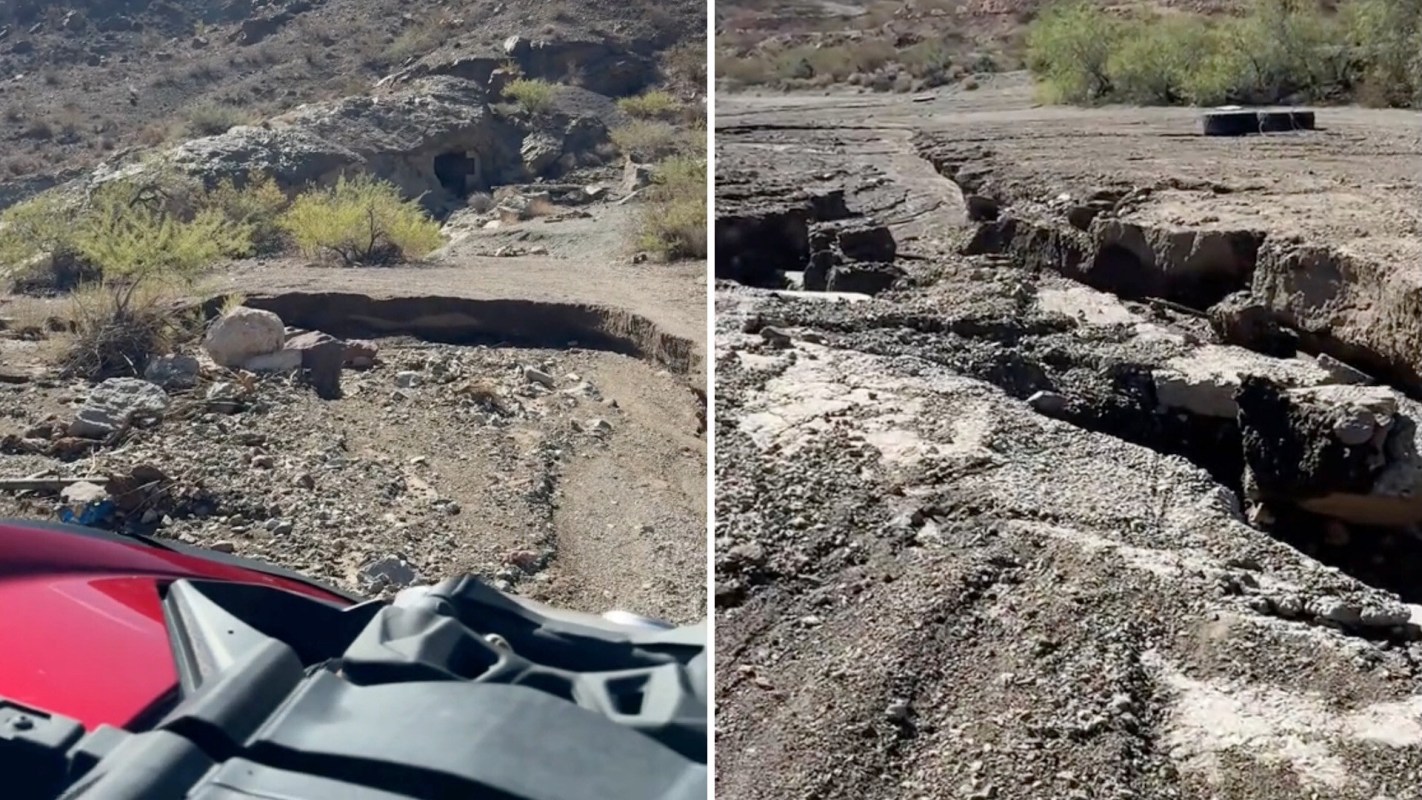 Cracks in the ground with rocky terrain and sparse vegetation in a dry landscape over a washed-out road.