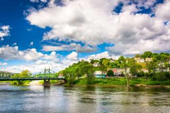 A green bridge crosses a river with a hillside of houses and trees under a blue sky filled with clouds.