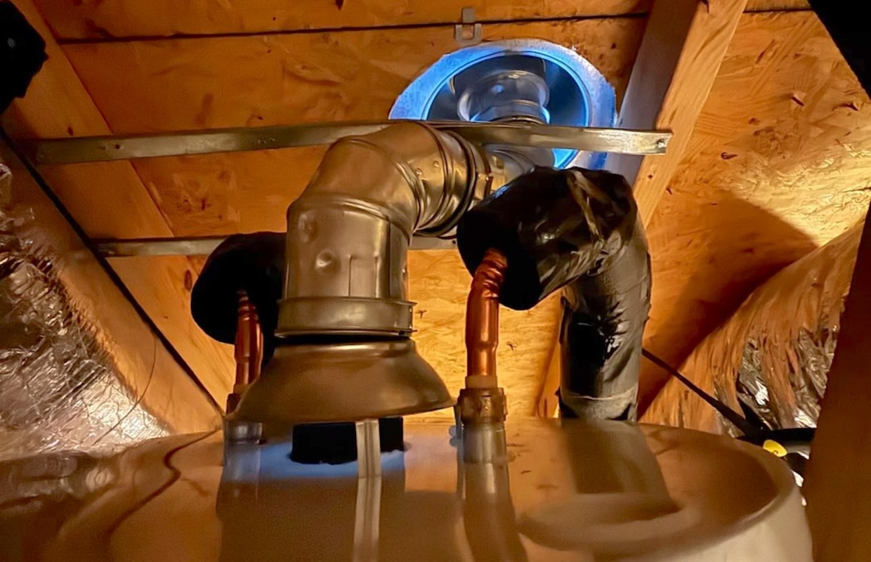 A plumbing setup with pipes and a vent in an attic space.
