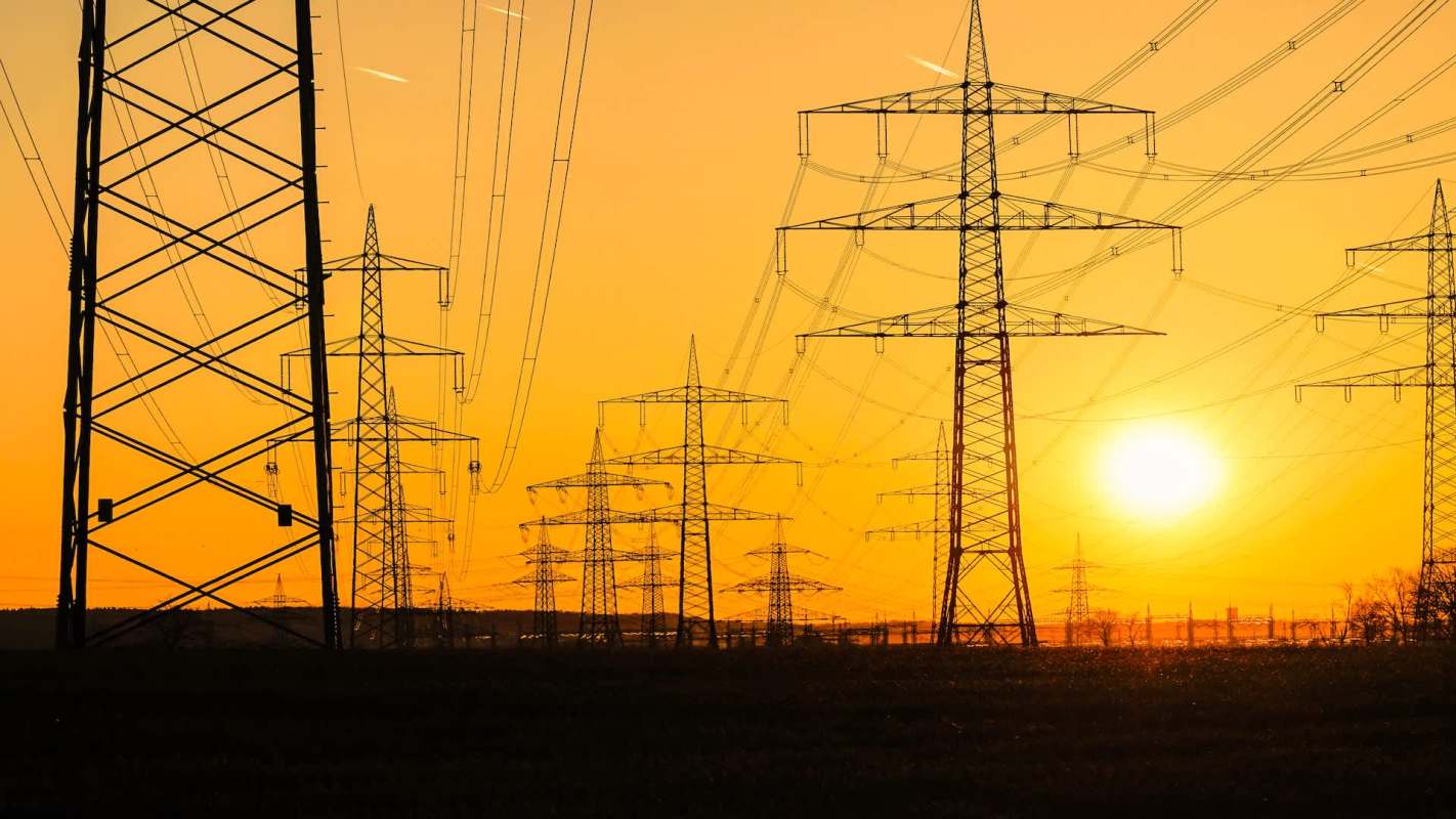 Silhouetted transmission towers and power lines at sunset.