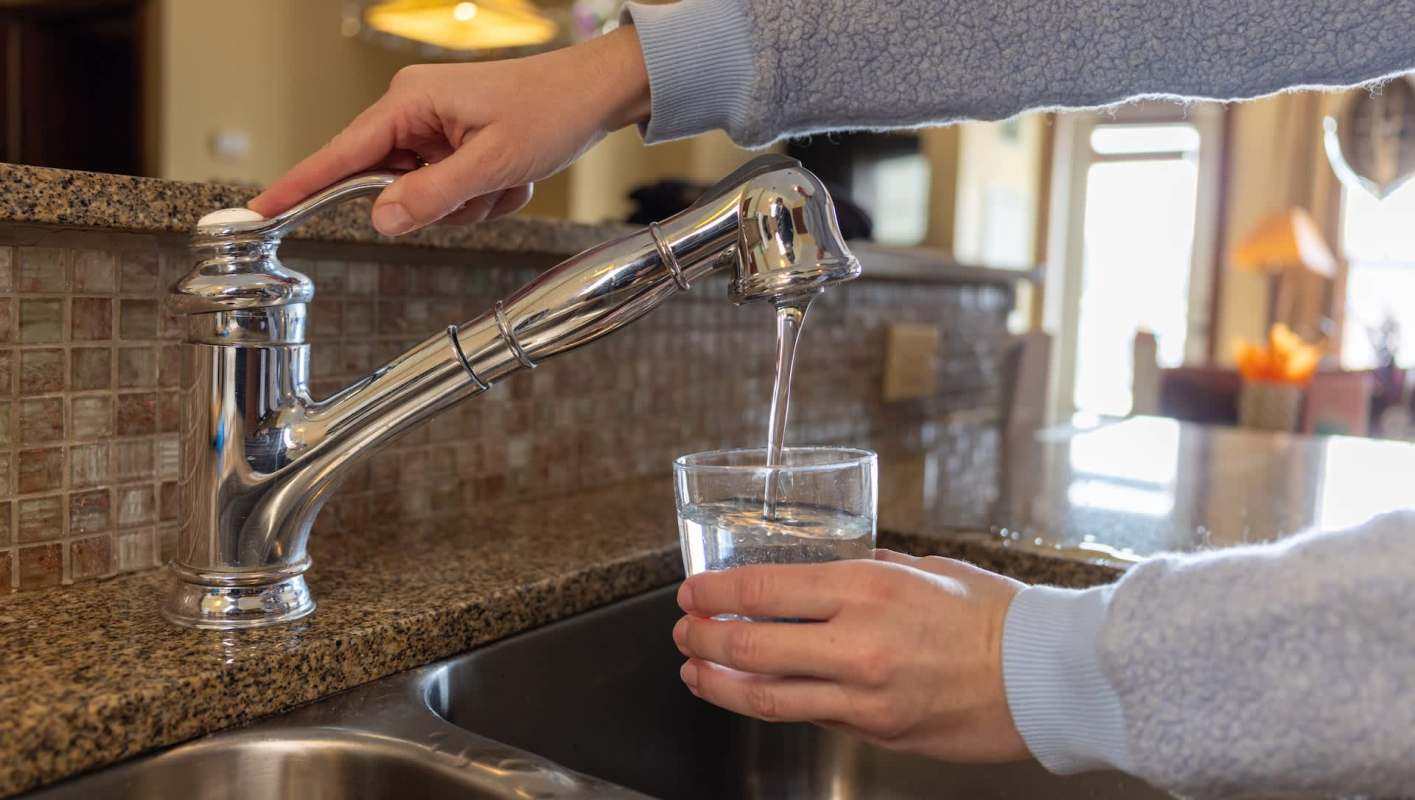 A hand fills a glass with water from a kitchen faucet.