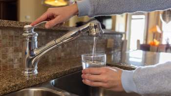 A hand fills a glass with water from a kitchen faucet.