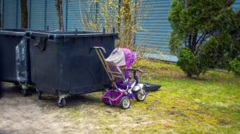 A small child's tricycle parked next to two large dumpsters in a grassy area.