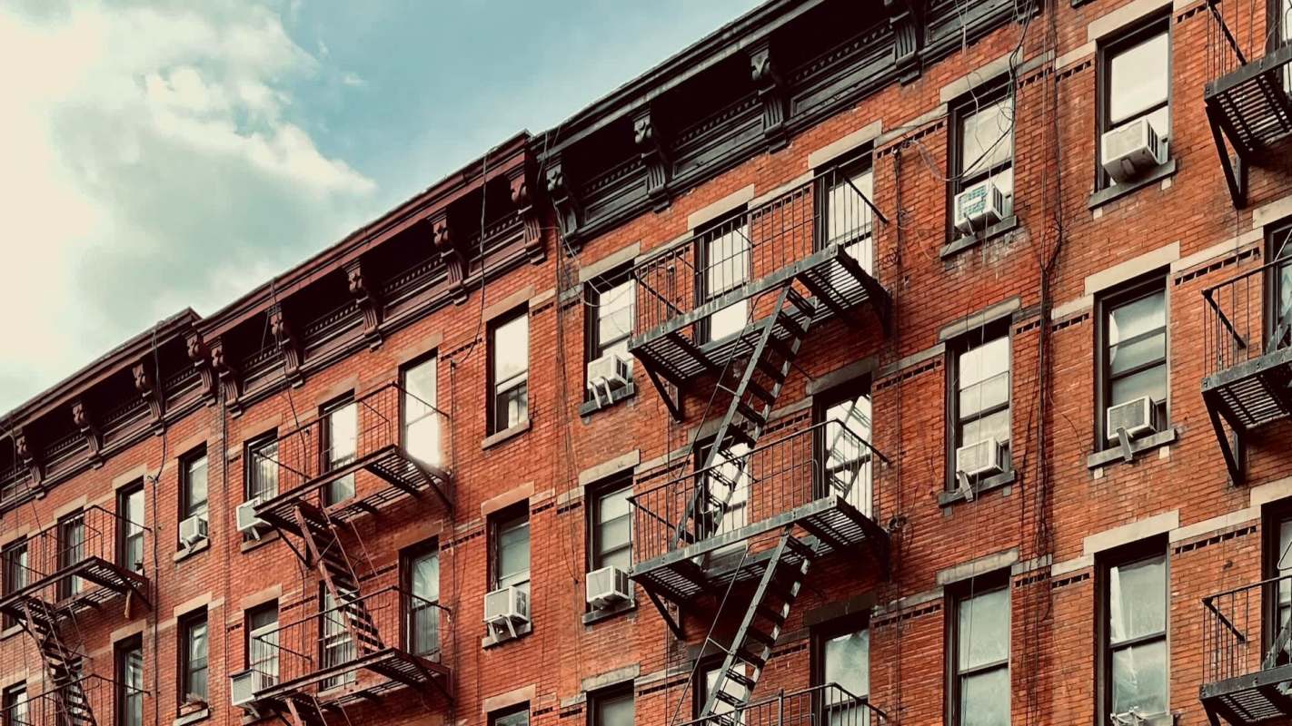 A brick apartment building with fire escapes and air conditioning units.