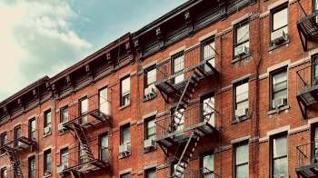 A brick apartment building with fire escapes and air conditioning units.