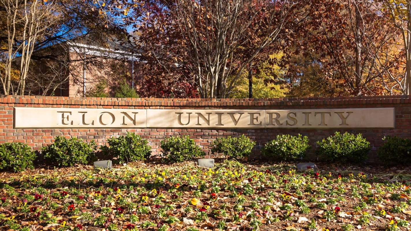 Elon University sign in front of a landscaped area with flowers and shrubs.