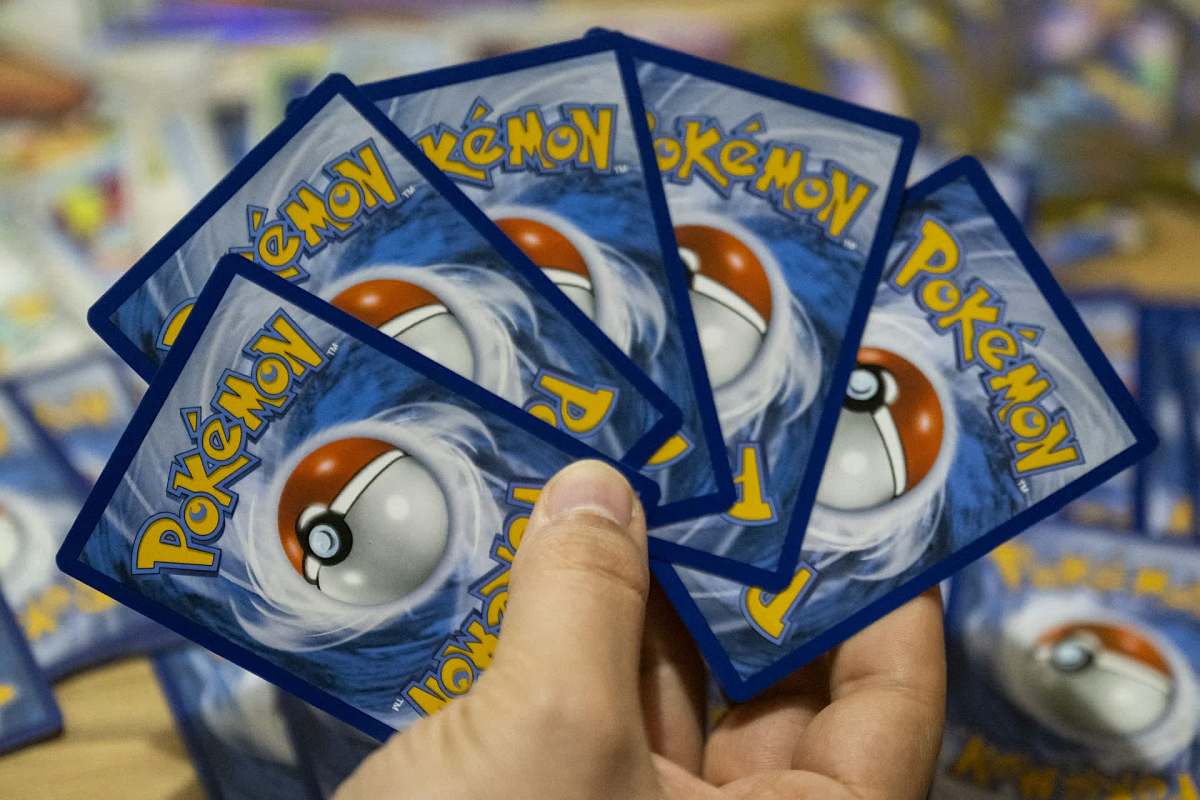 A hand holds several Pokémon trading cards with a design featuring a Poké Ball.