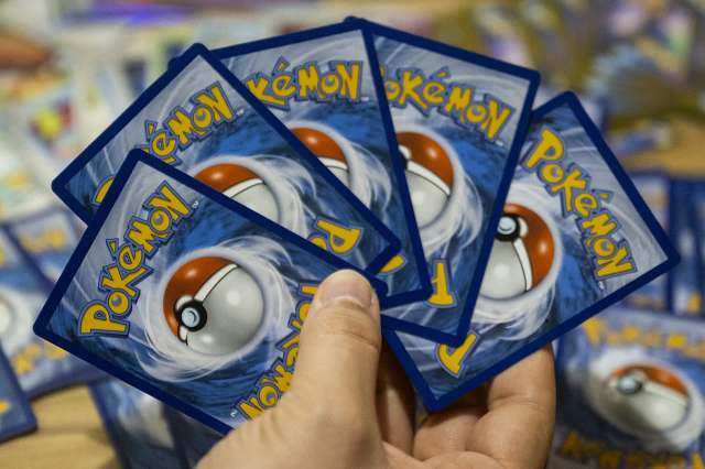 A hand holds several Pokémon trading cards with a design featuring a Poké Ball.