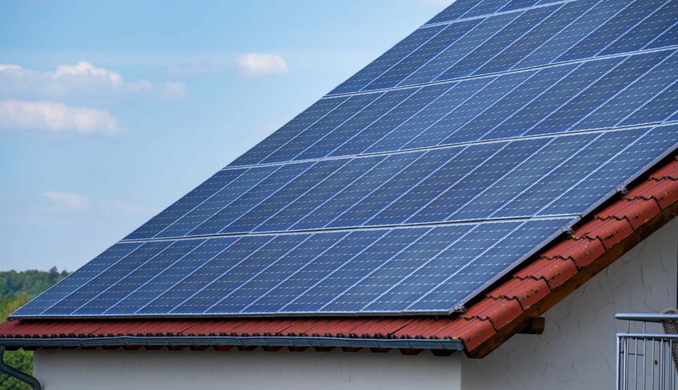 A rooftop covered with solar panels against a blue sky with clouds.