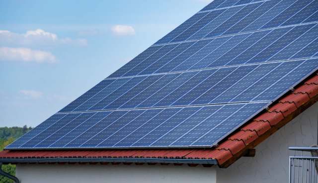 A rooftop covered with solar panels against a blue sky with clouds.