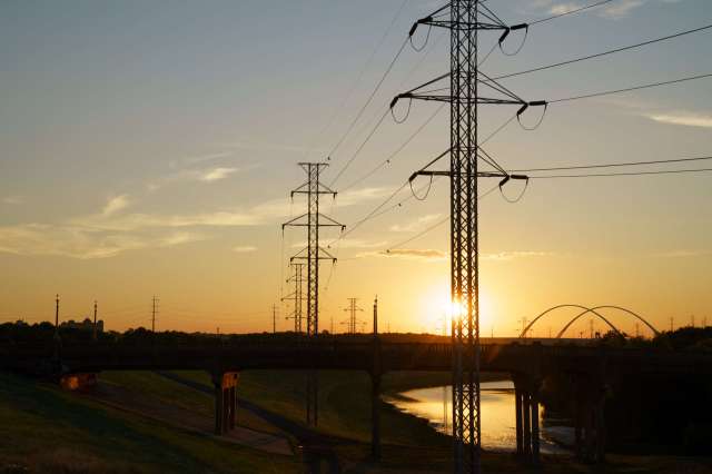 Power lines and a bridge extend over a river at sunset, with a colorful sky in the background.