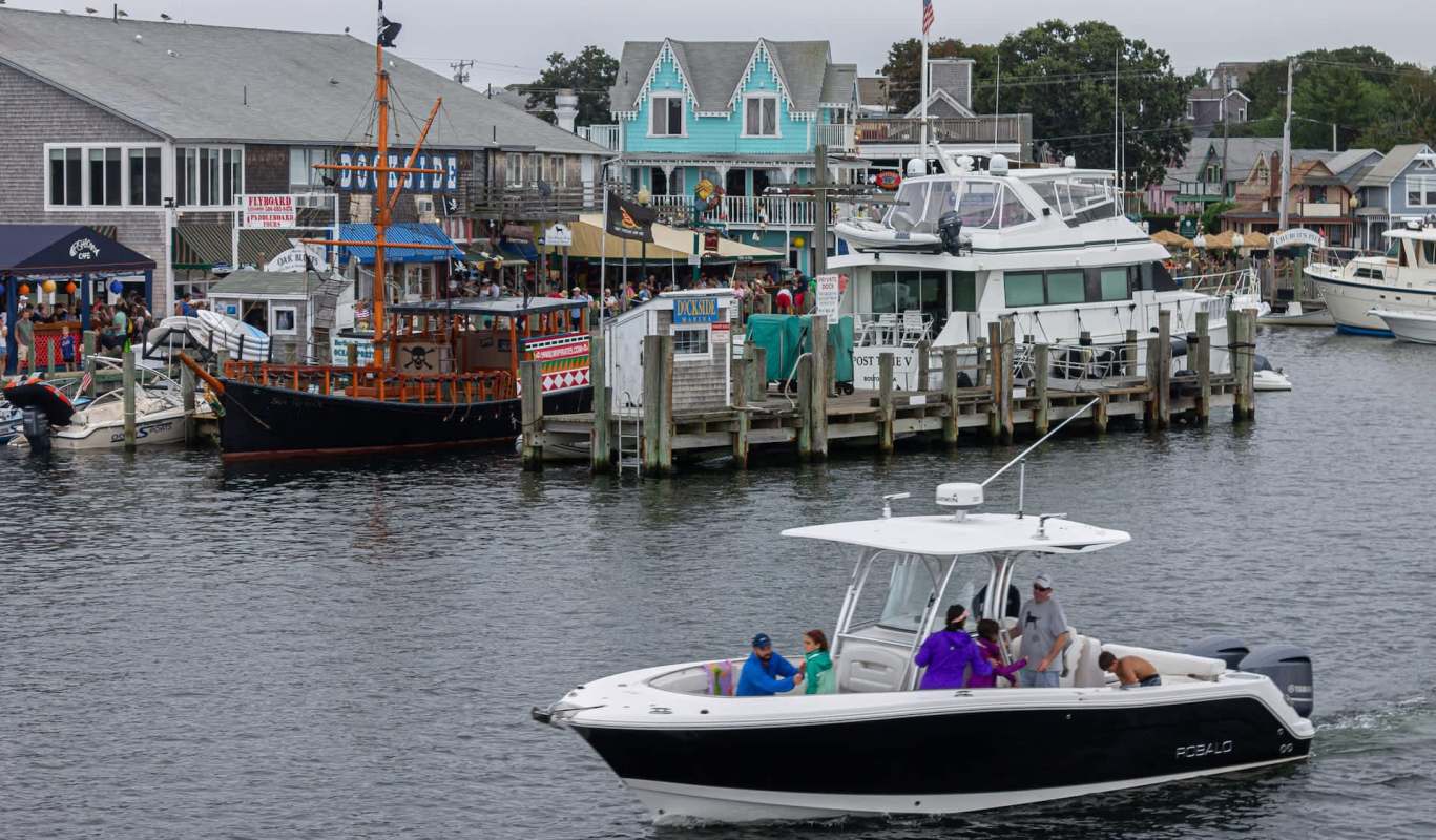 A marina scene with boats and colorful buildings filled with people along the waterfront.