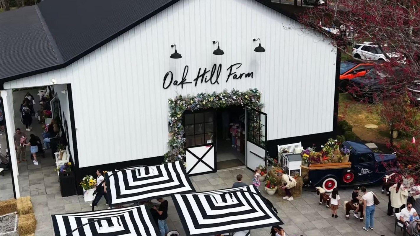 A farm building with a sign reading "Oak Hill Farm," surrounded by people and colorful decorations.