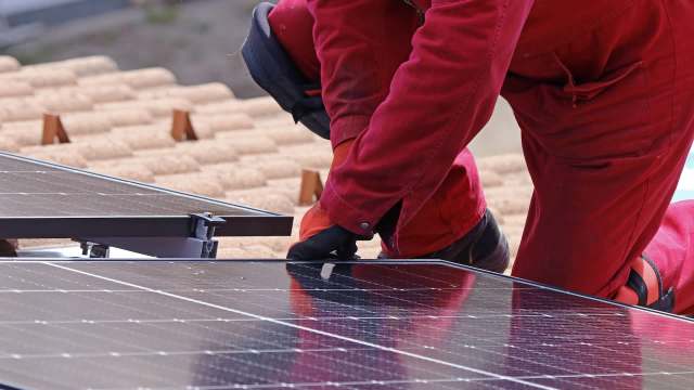 A worker installs solar panels on a rooftop.