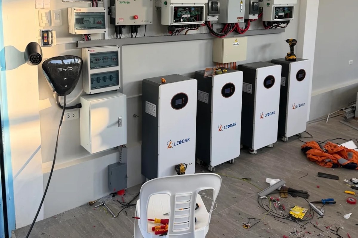 A wall-mounted setup of energy storage batteries and electrical equipment with scattered tools on the floor.